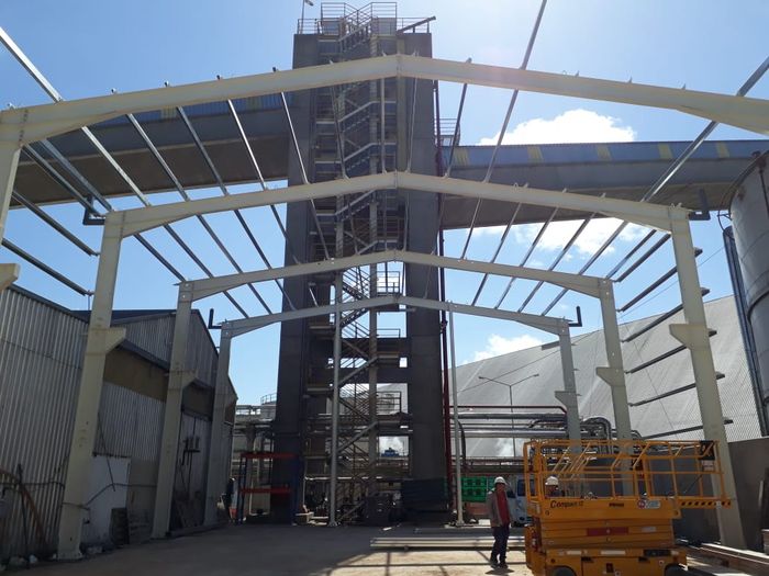 Estructura metálica en montaje junto a torre de proceso industrial, obra de Amione Construcciones